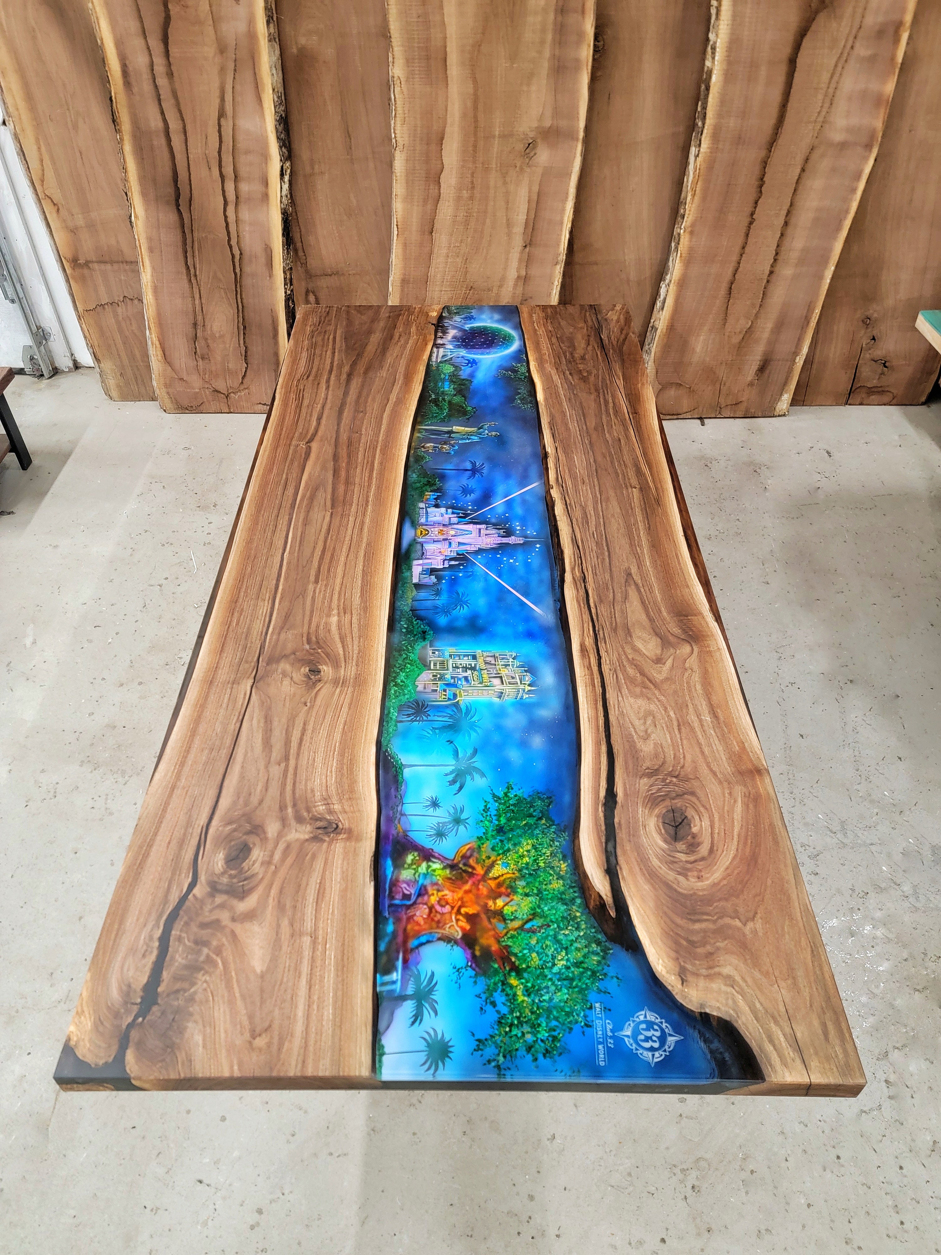 Custom wooden table with epoxy covering an airbrush scene of the Walt Disney parks (Cinderalla's castle, Tree of Life, Hollywood House of Terror, Epcot, and the Statue of Mickey Mouse and Walt Disney) built by Backyard Resin.