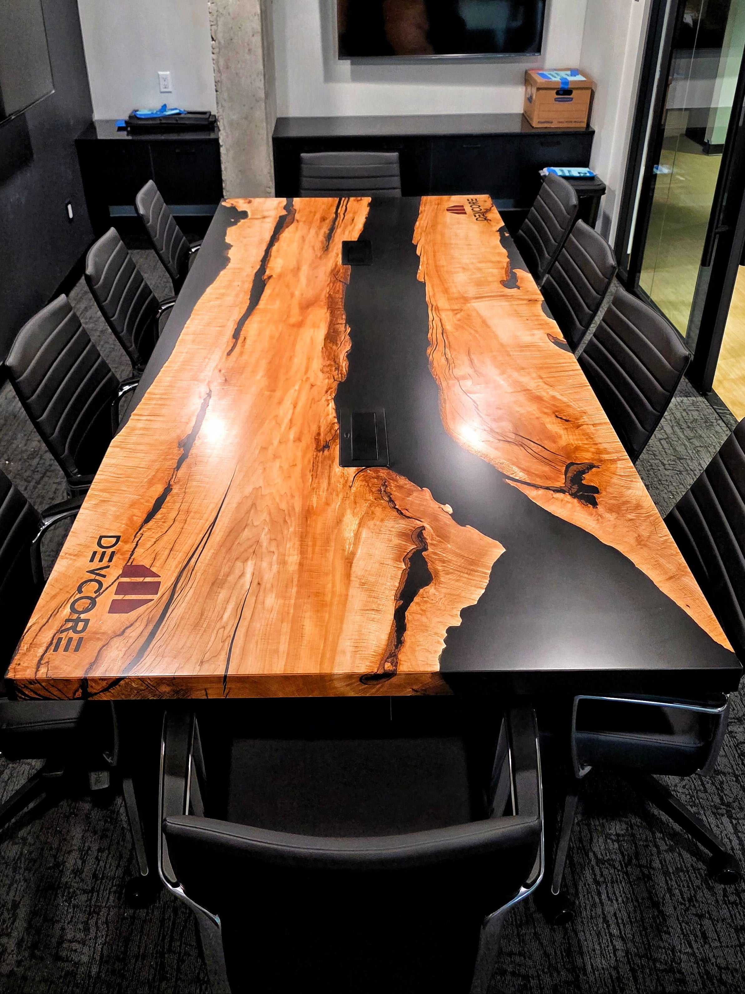 Maple conference table with black rivers of epoxy, central wireless charging ports, engraved company logo that read 'Devcore'